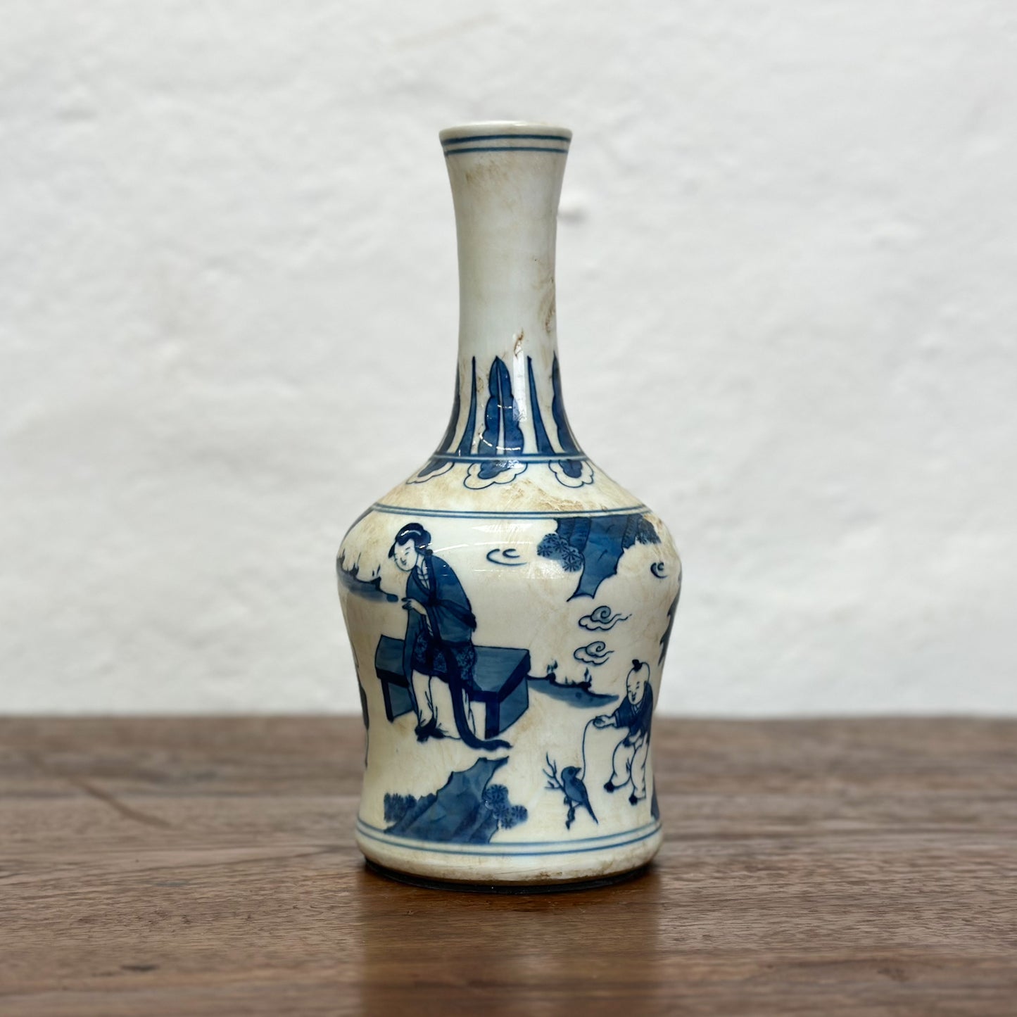 A blue and white porcelain vase with figural long neck design, depicting characters in a traditional setting.