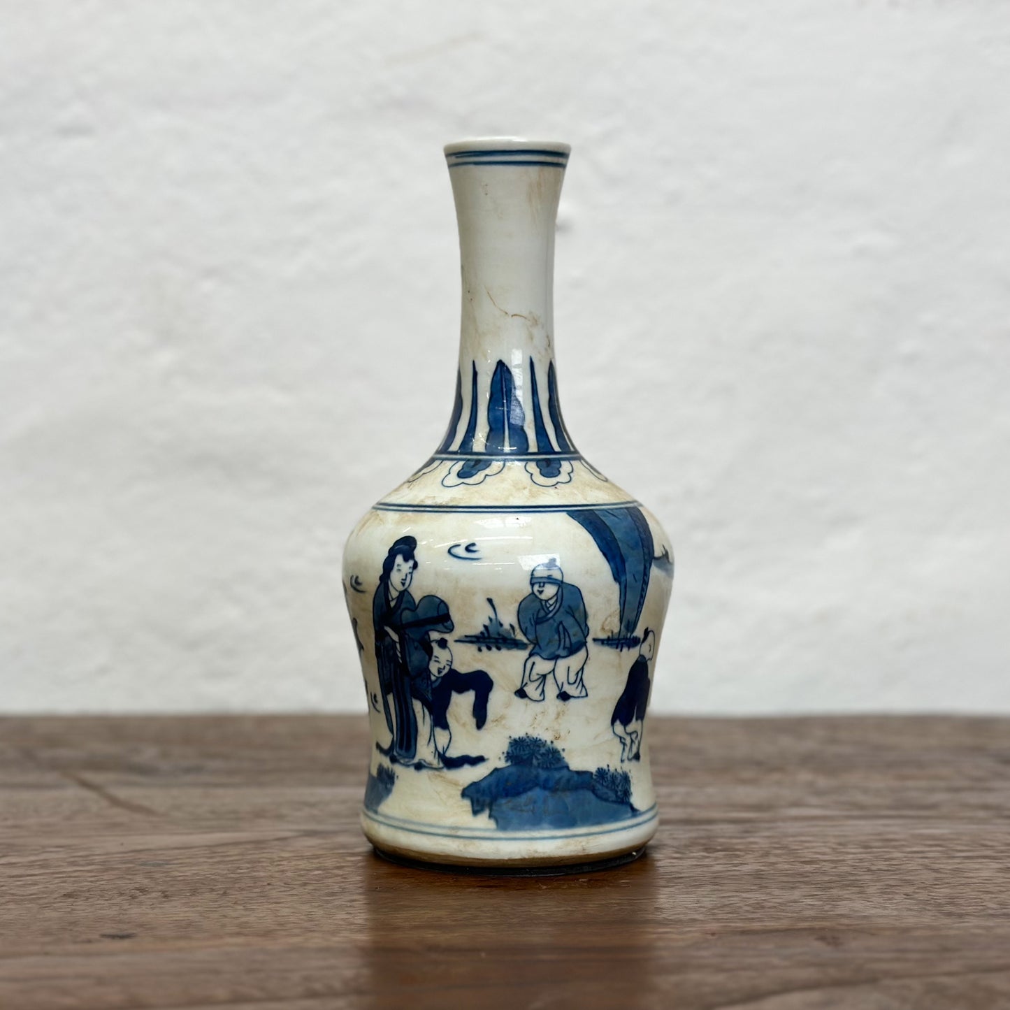 A blue and white porcelain vase with figural long neck design, depicting characters in a traditional setting.