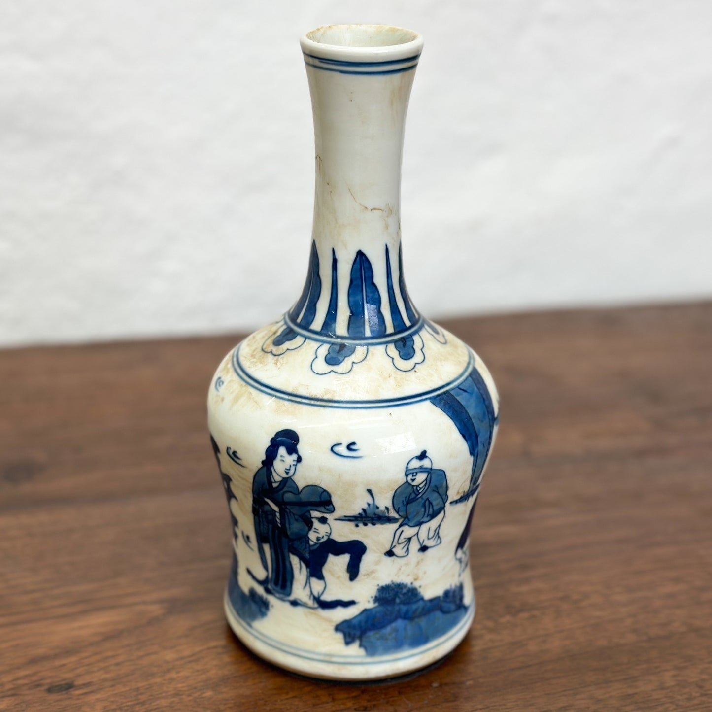 A blue and white porcelain vase with figural long neck design, depicting characters in a traditional setting.