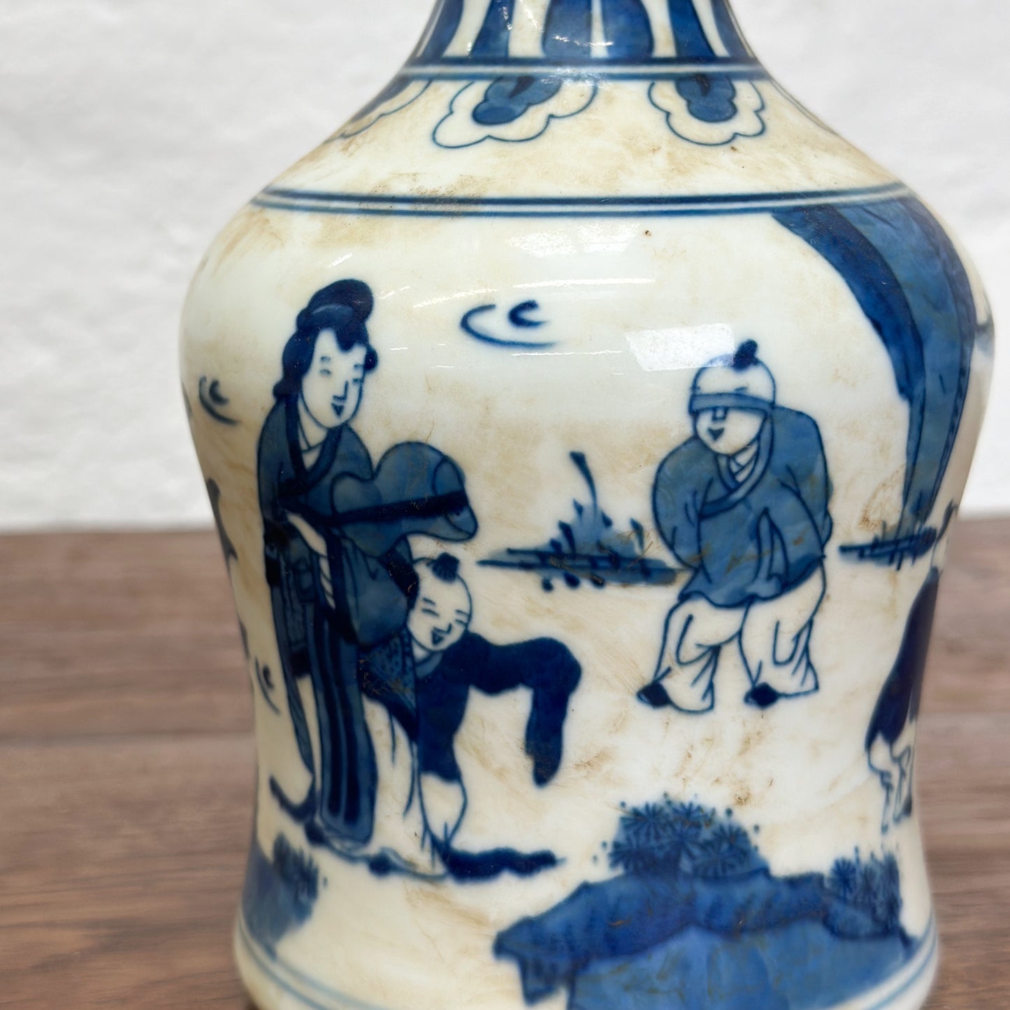 A blue and white porcelain vase with figural long neck design, depicting characters in a traditional setting.