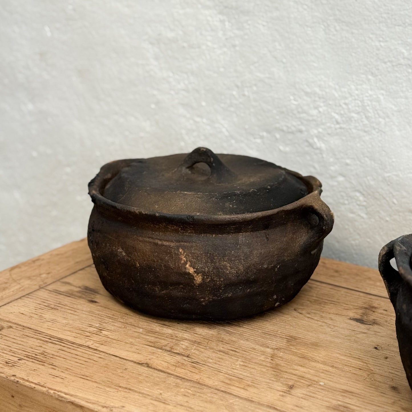 Vintage black pot with lid on a wooden surface against a white wall