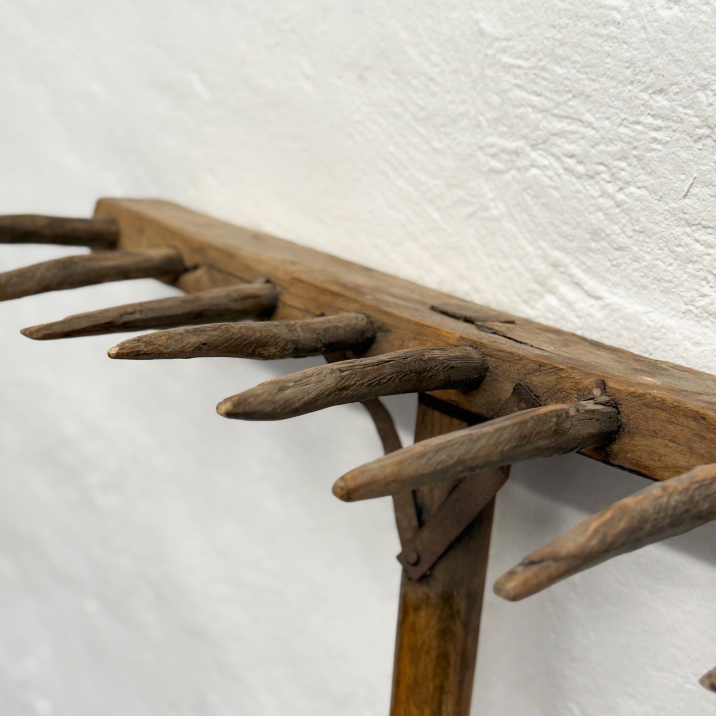 Wooden rake with metal tines against a white wall