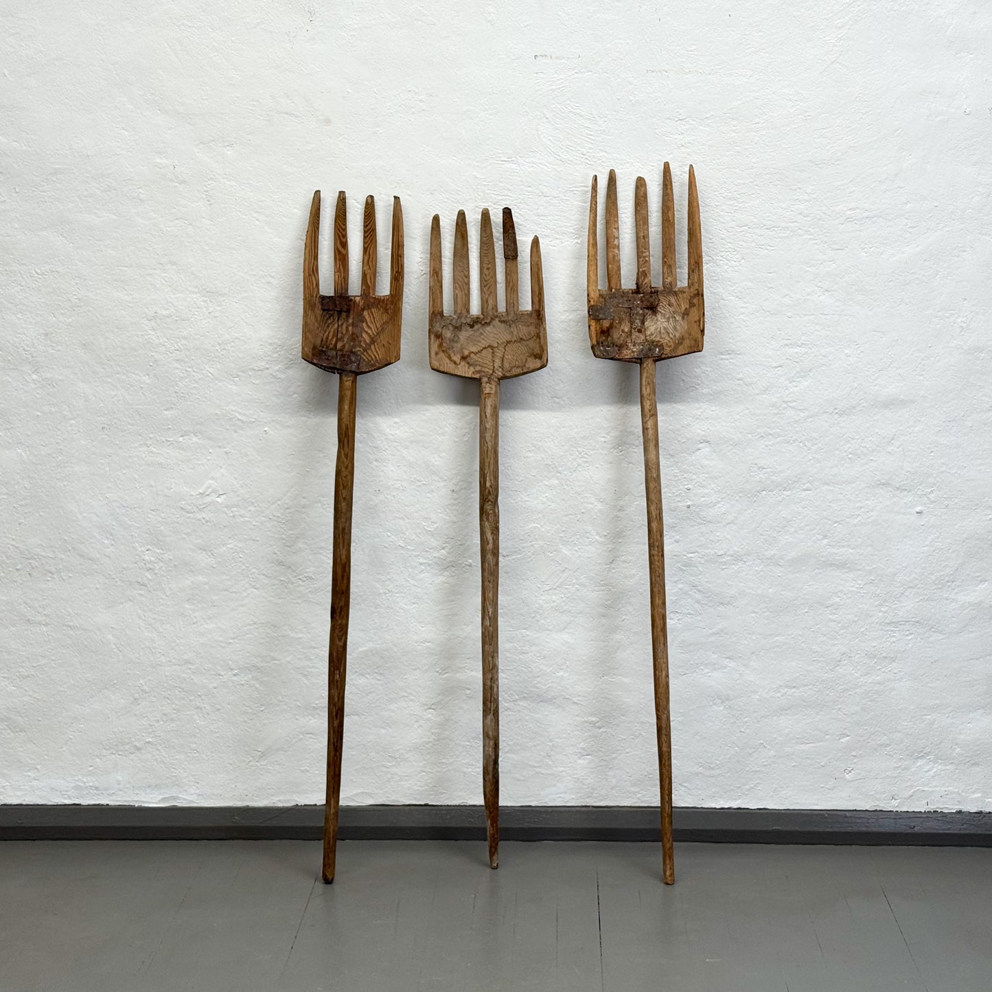 Three wooden forks of varying sizes against a textured white wall.