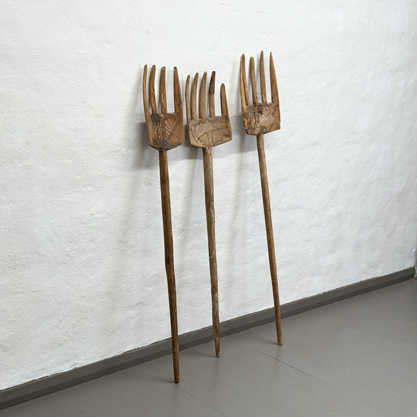 Three wooden garden forks leaning against a textured white wall.