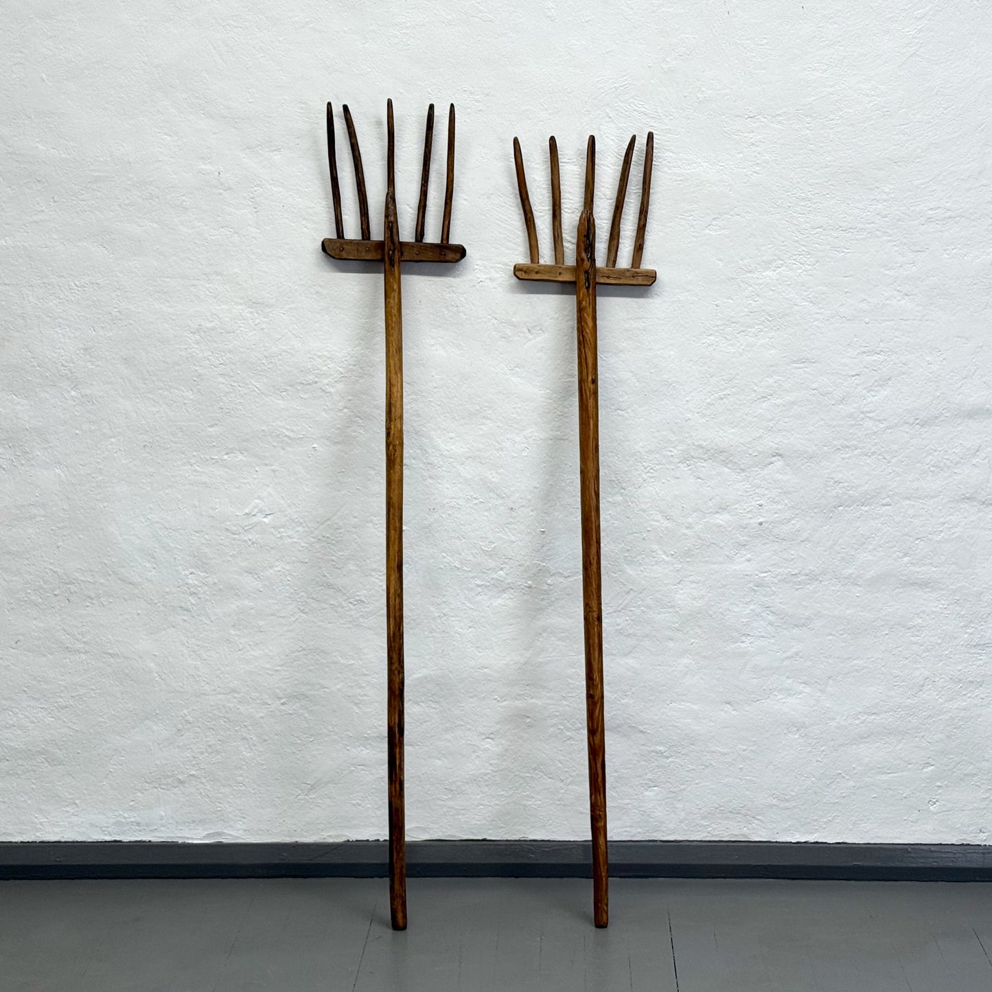 Two wooden rakes against a white textured wall.