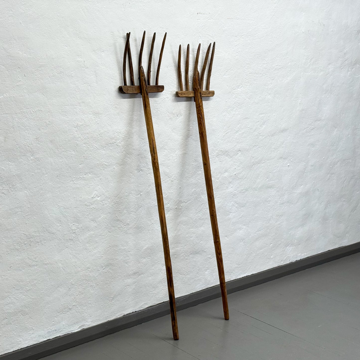Two wooden rakes leaning against a textured white wall.