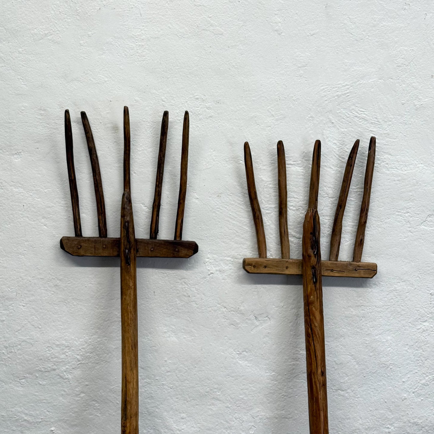 Two wooden hay forks on a textured white background