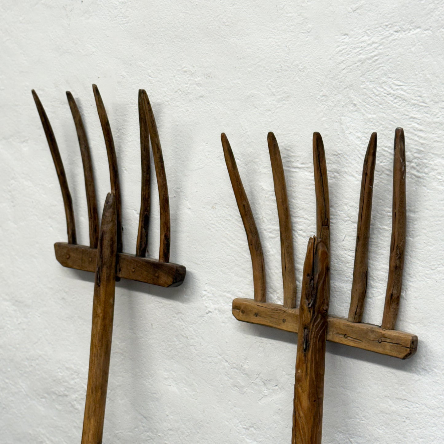 Two wooden garden forks against a white textured wall
