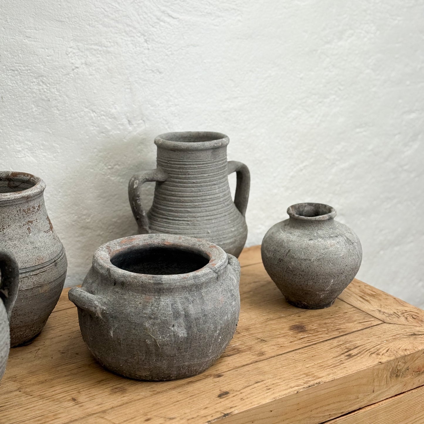 Four rustic clay pots on a wooden surface with a textured white wall background