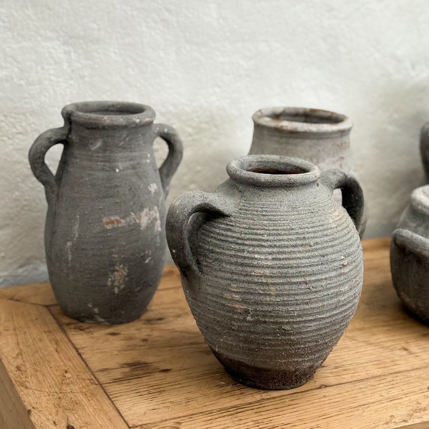 Three rustic clay pots on a wooden surface with a white textured wall background.