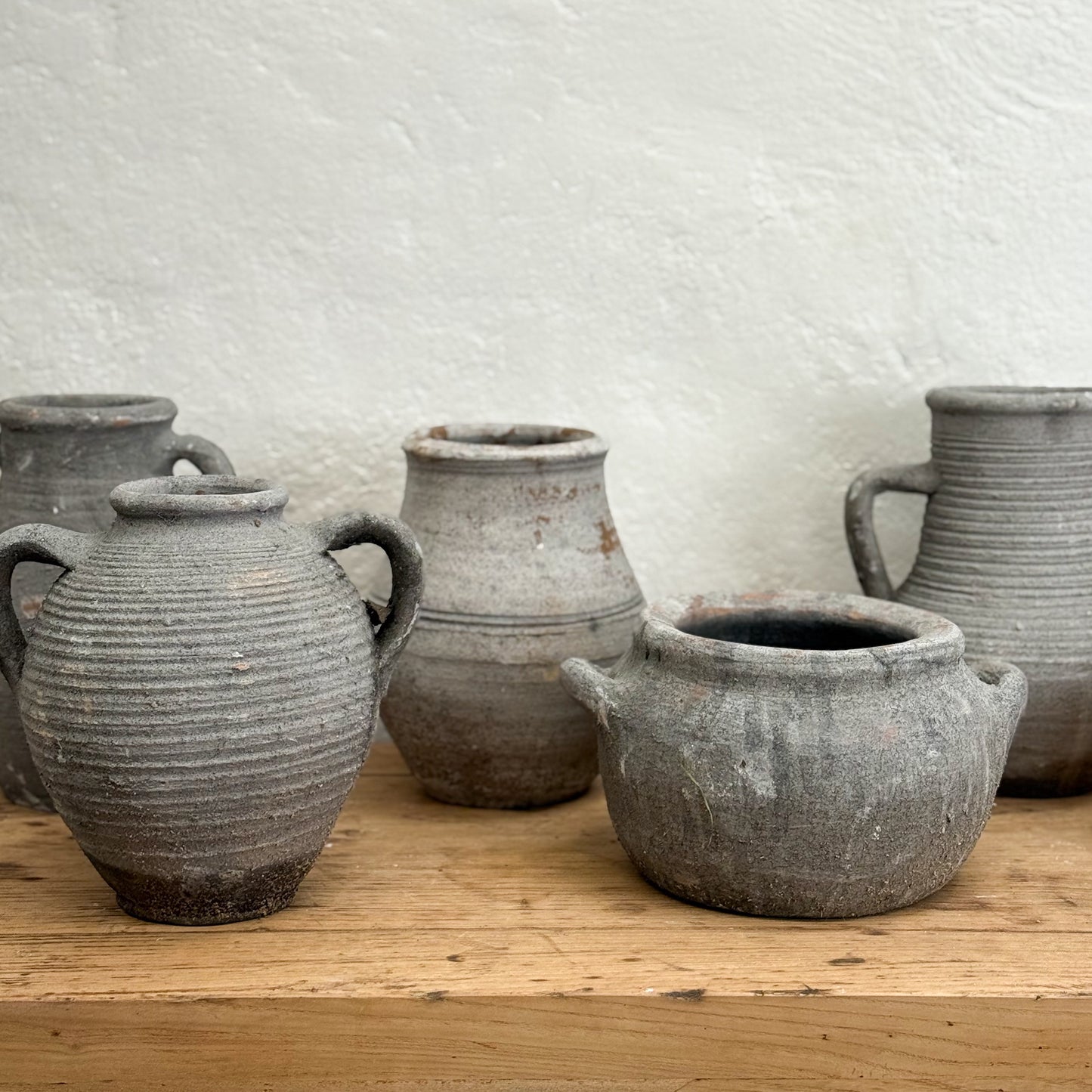 Set of rustic clay pots on a wooden surface with a textured white wall background
