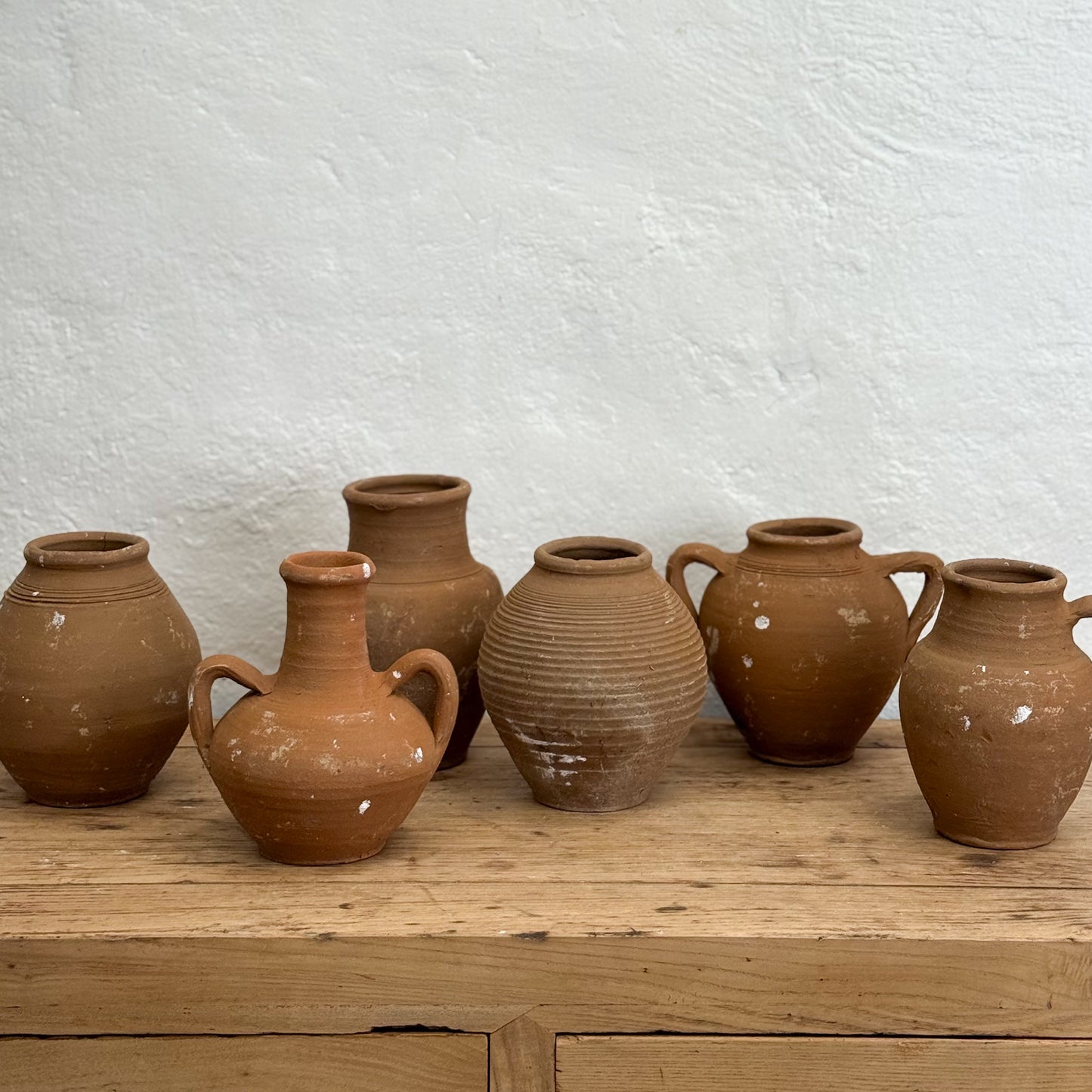Set of terracotta pots on a wooden surface with a white textured wall background