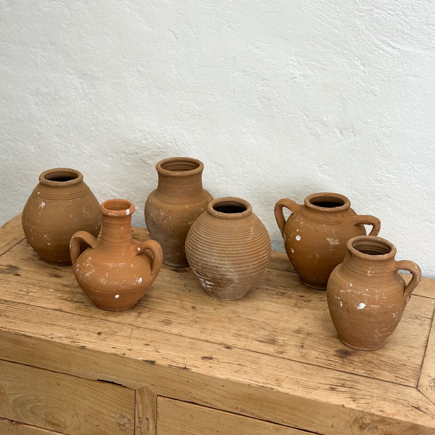 Set of terracotta pots on a wooden surface with a white textured wall background