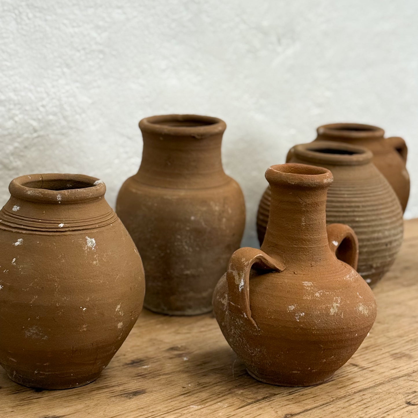 Set of terracotta pots on a wooden surface with a textured white wall background