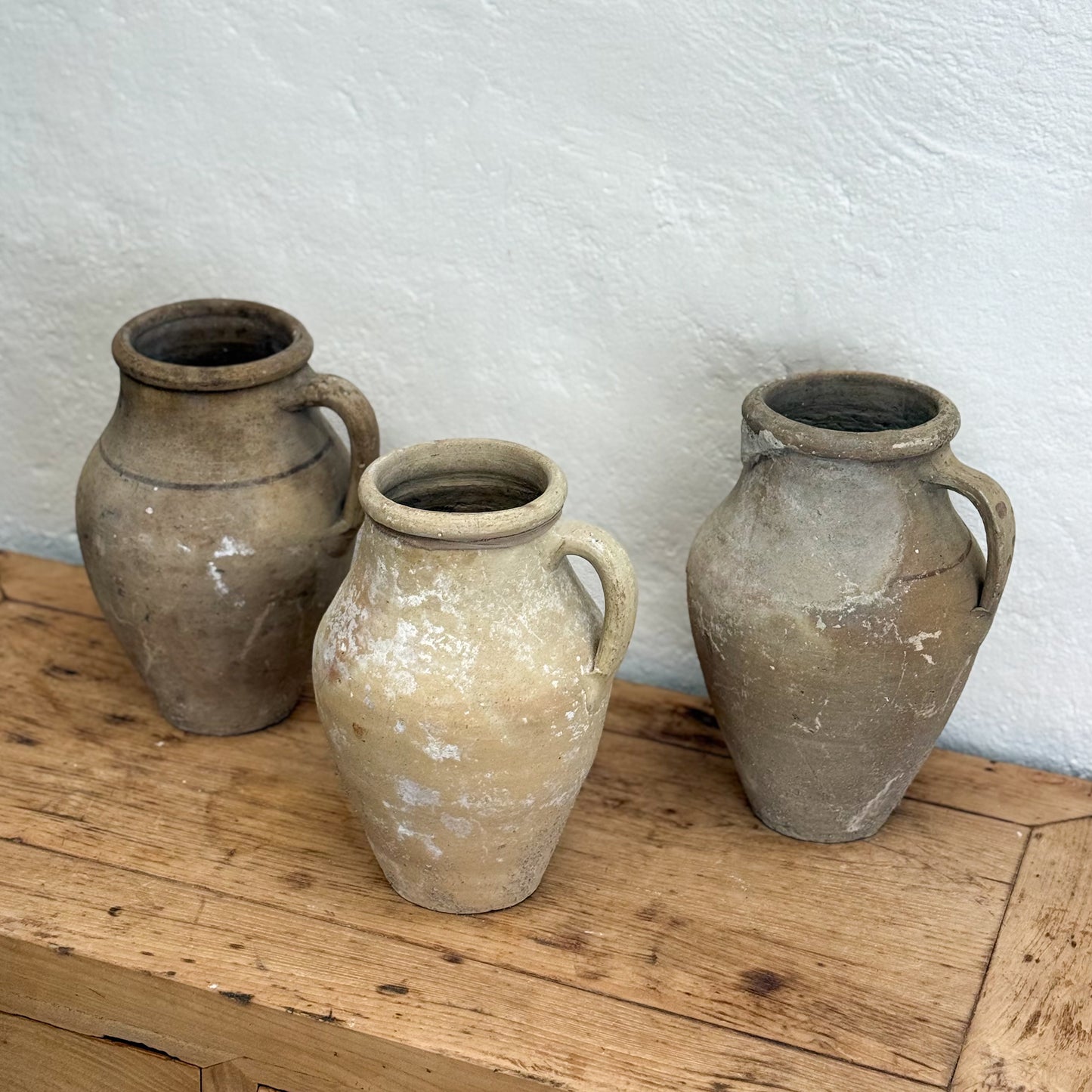 Three rustic clay pots on a wooden surface with a white textured wall background.