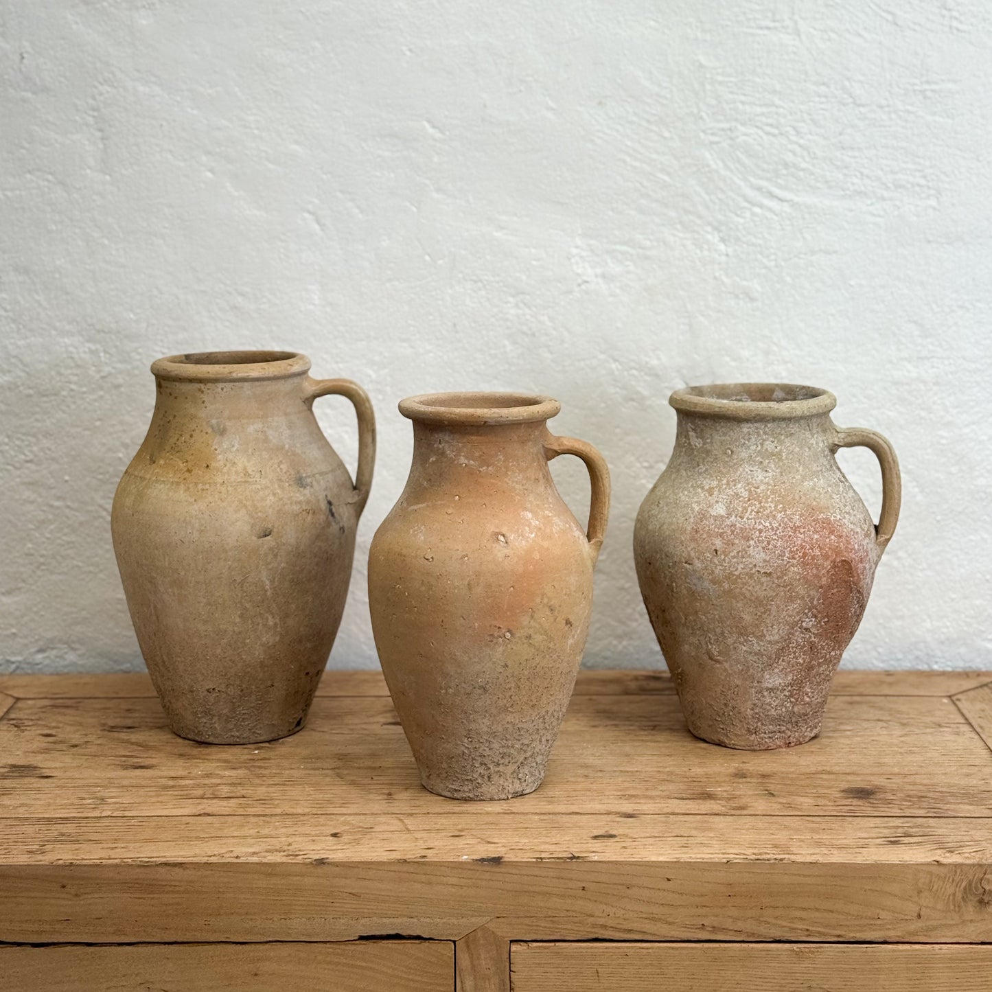 Three terracotta vases on a wooden surface with a textured white wall background