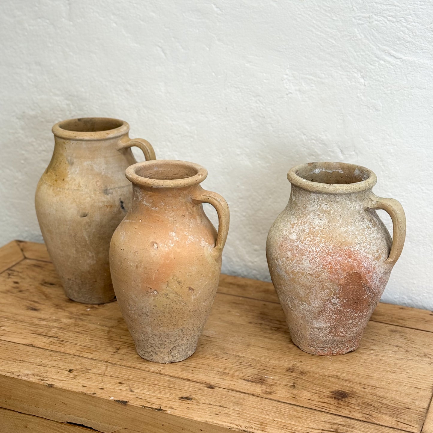 Three terracotta vases on a wooden surface with a white textured wall background