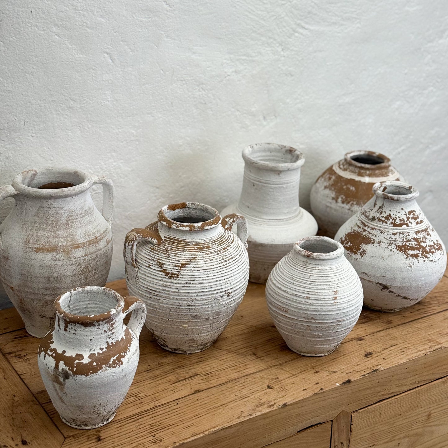 Set of rustic ceramic pots on a wooden surface with a white wall background