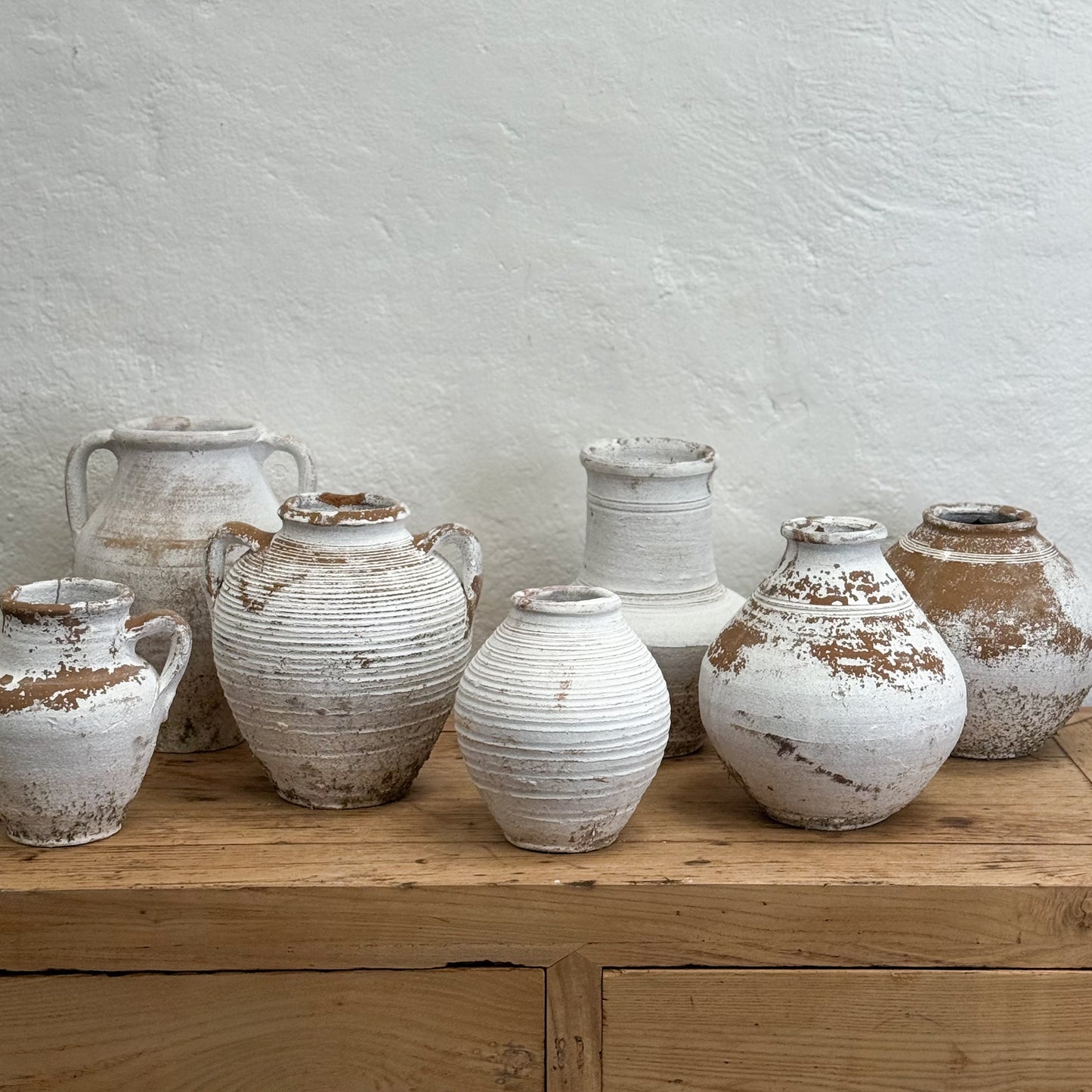Set of rustic ceramic jars on a wooden surface with a light gray wall background