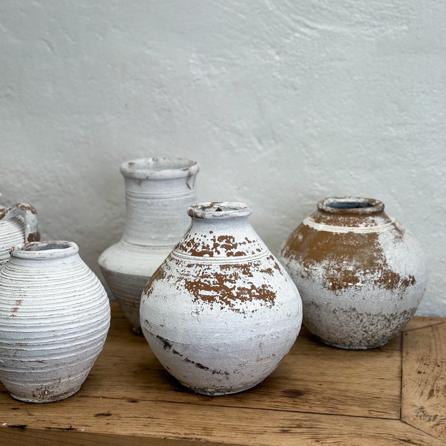 Set of rustic ceramic vases on a wooden surface with a light gray wall background