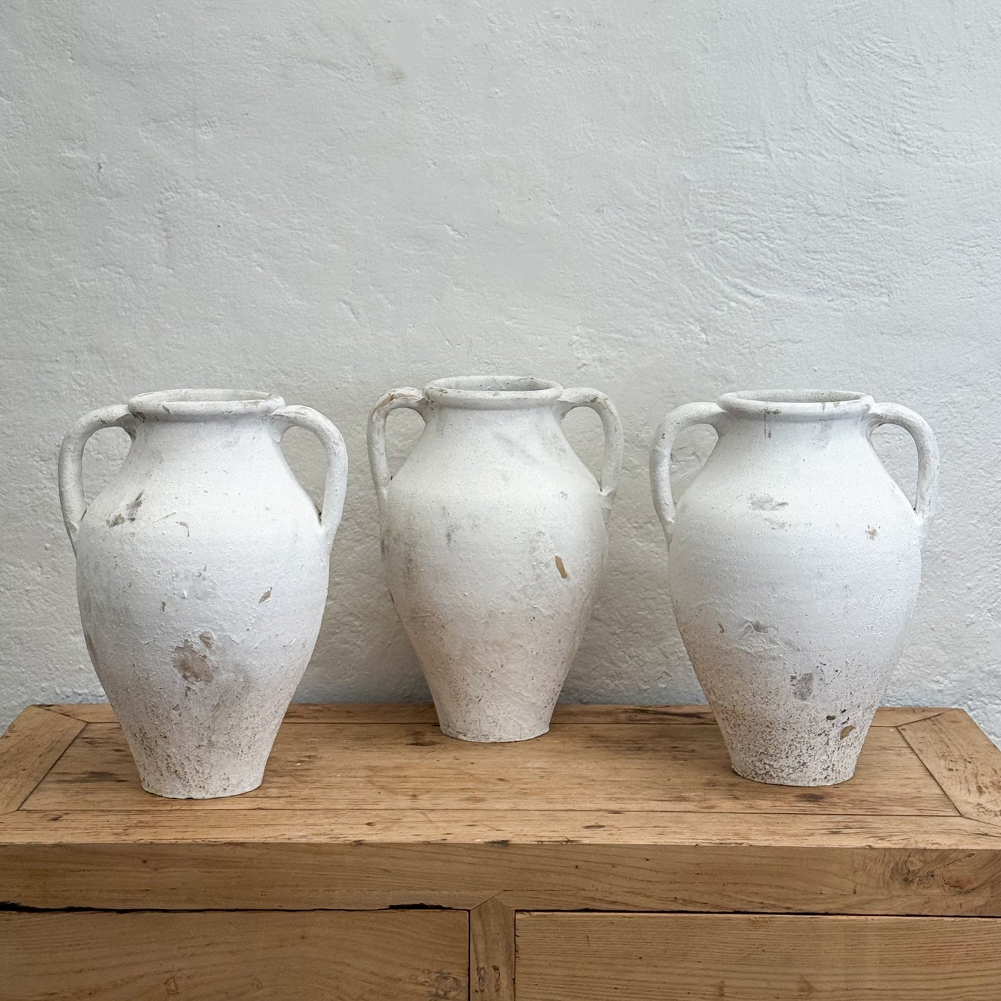 Three white ceramic urns on a wooden surface with a light gray wall background