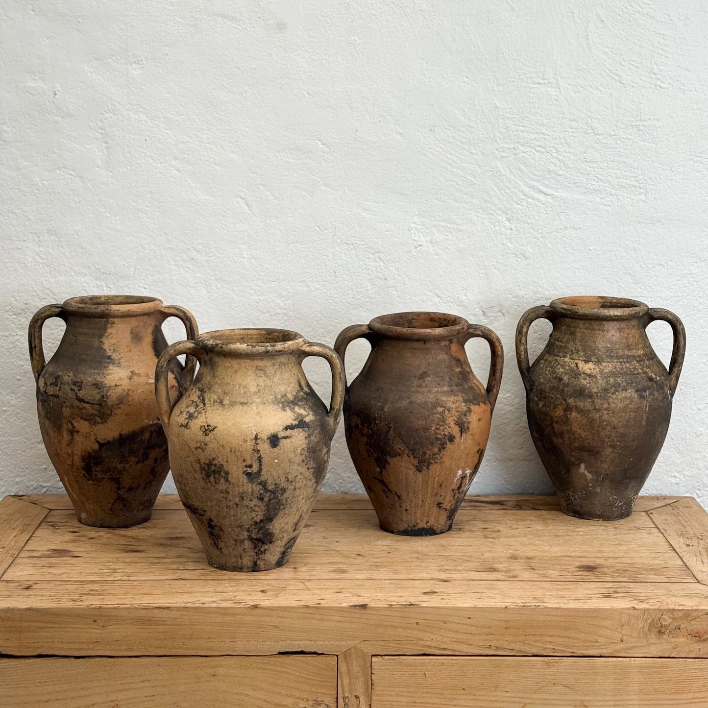 Four rustic clay pots on a wooden surface with a white textured wall background