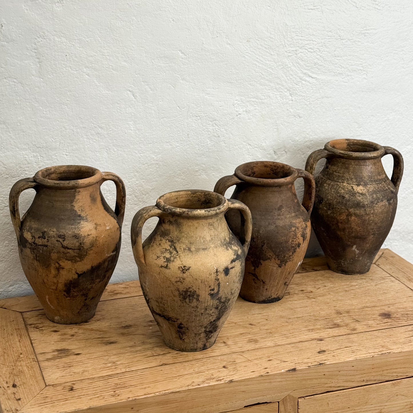 Four rustic clay pots on a wooden surface with a white wall background