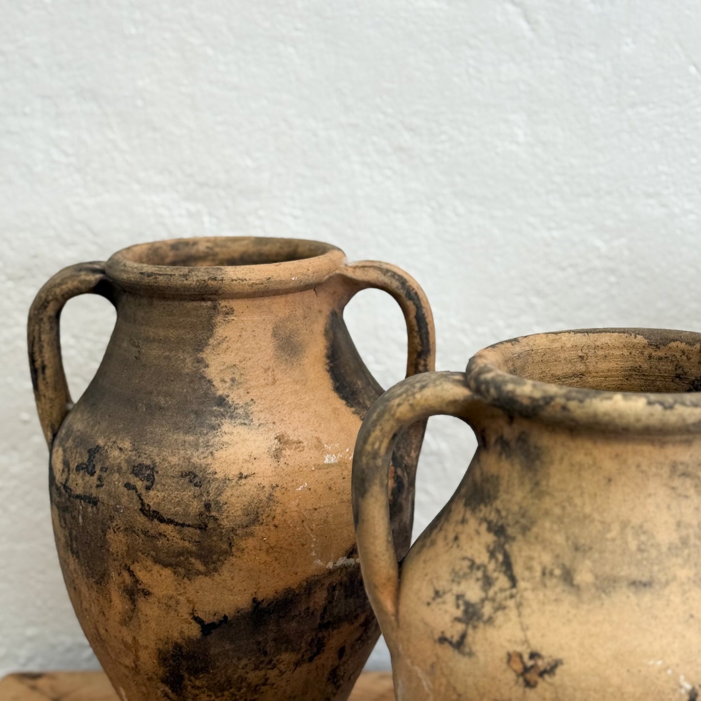 Two rustic clay pots with handles on a textured white background