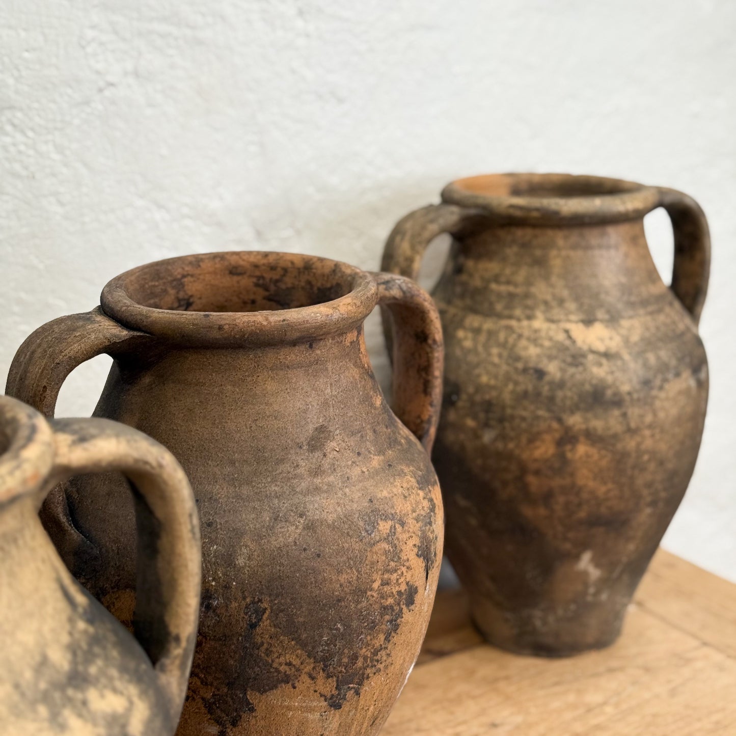 Three rustic clay pots on a wooden surface with a light gray background