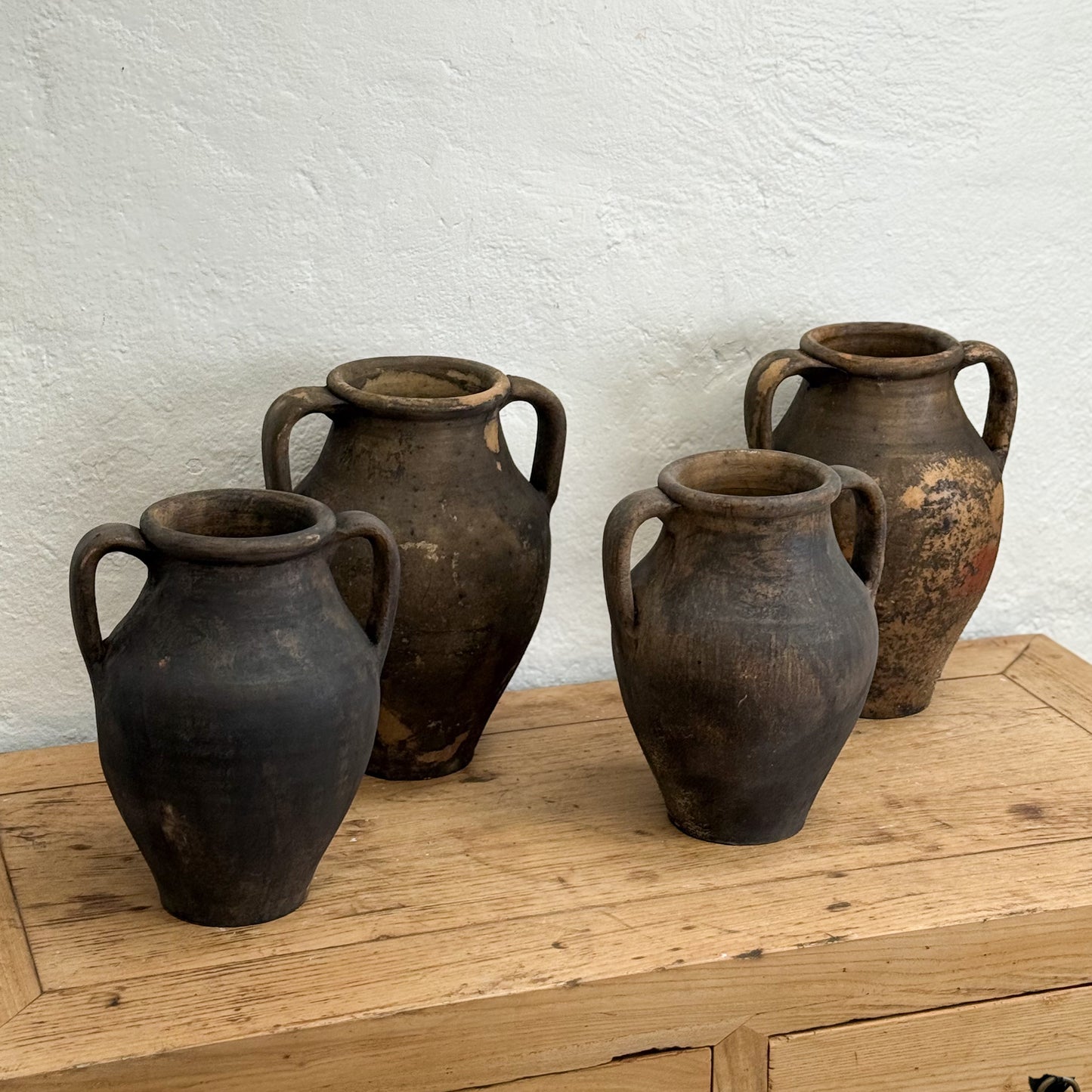 Four rustic clay pots on a wooden surface with a white textured wall background