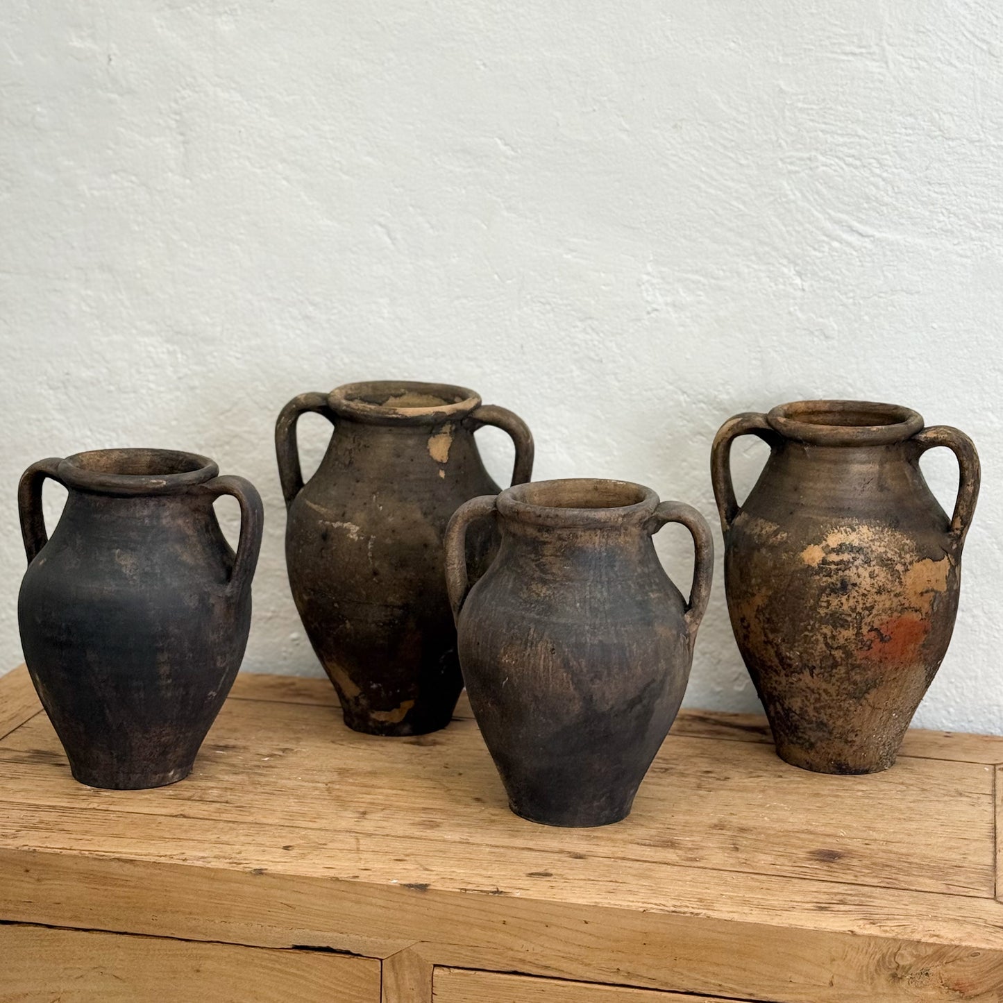 Four rustic clay pots on a wooden surface with a white textured wall background