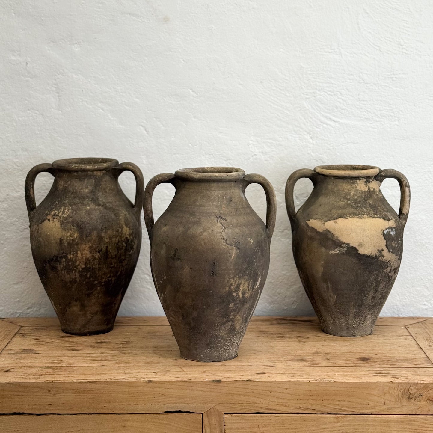 Three rustic clay pots on a wooden surface with a white textured wall background