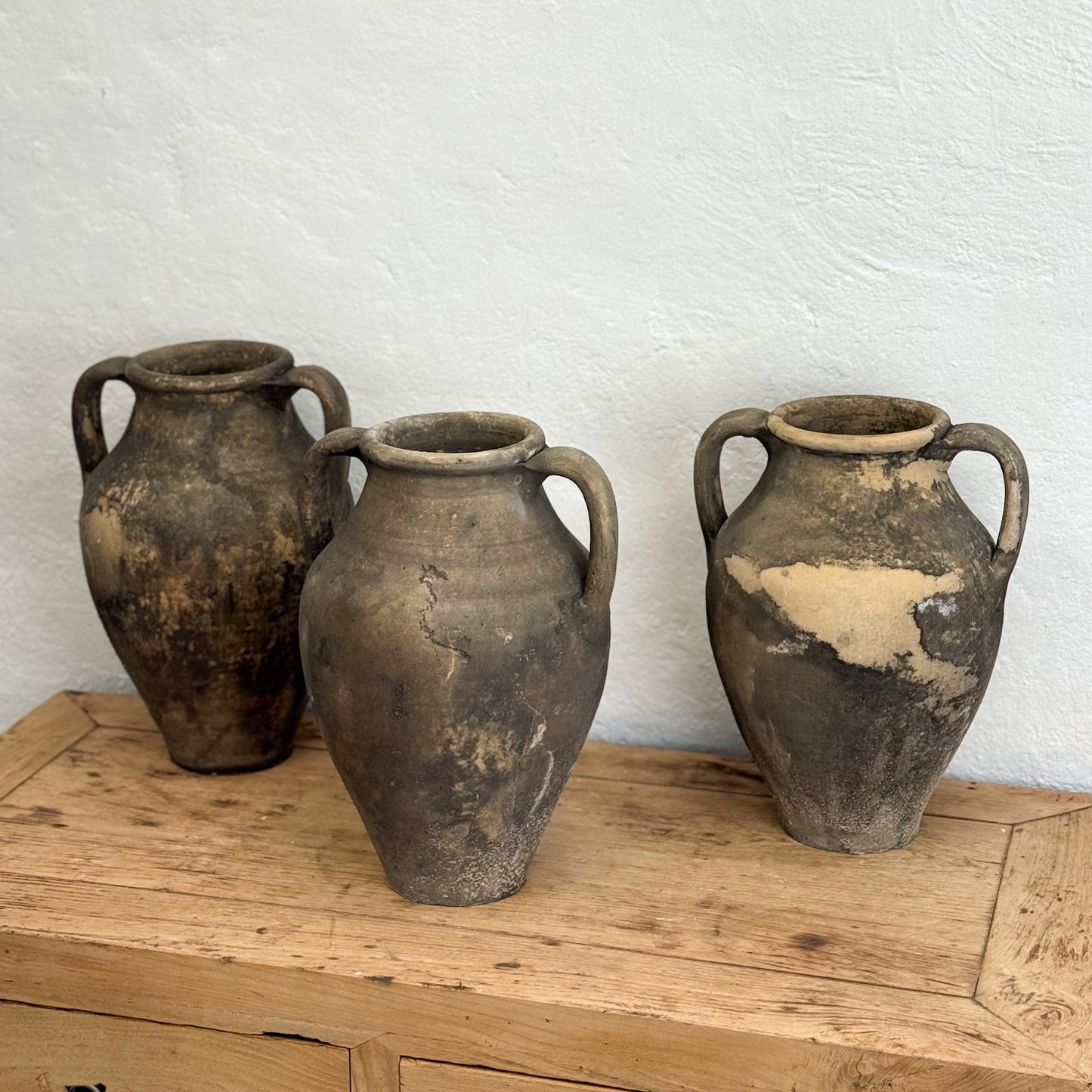 Three rustic clay pots on a wooden surface with a white wall background