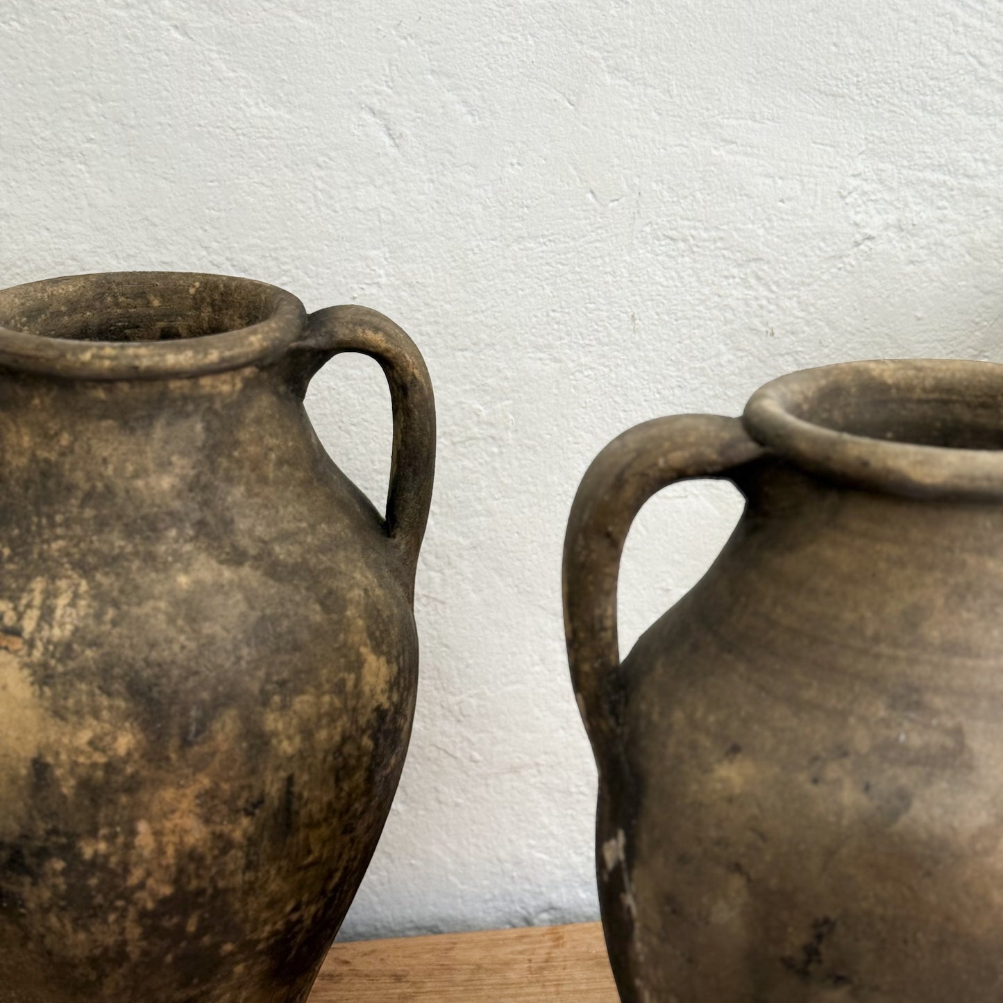 Two rustic clay pots on a wooden surface with a white textured wall background.