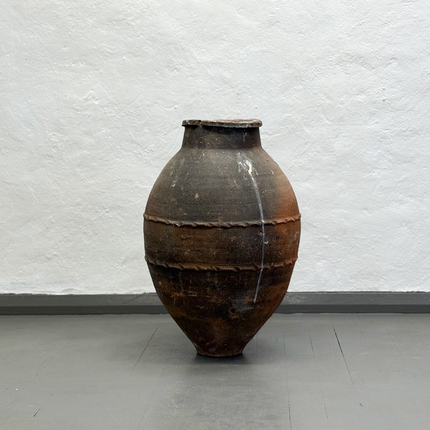 Vintage terracotta pot on a plain floor with a light gray wall background