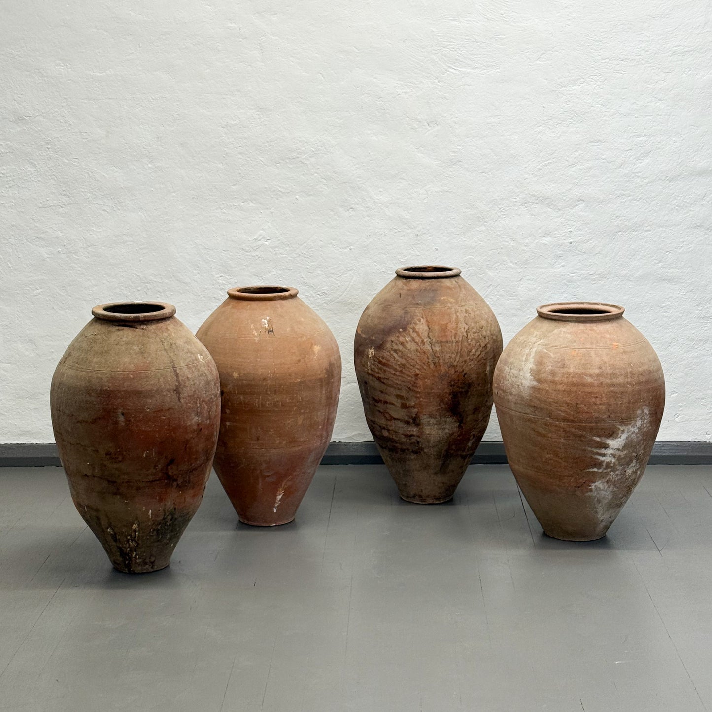 Four large terracotta pots against a textured white wall.