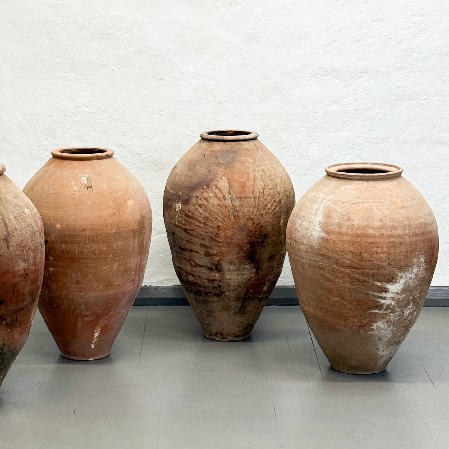 Four large terracotta pots against a light gray wall.