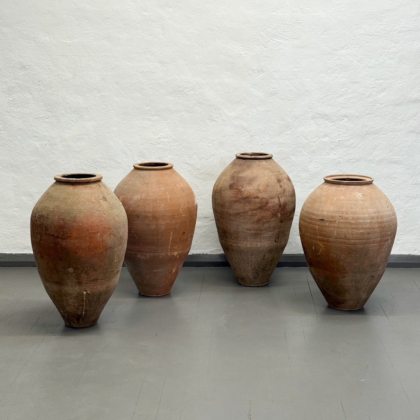 Four large terracotta pots against a textured white wall.