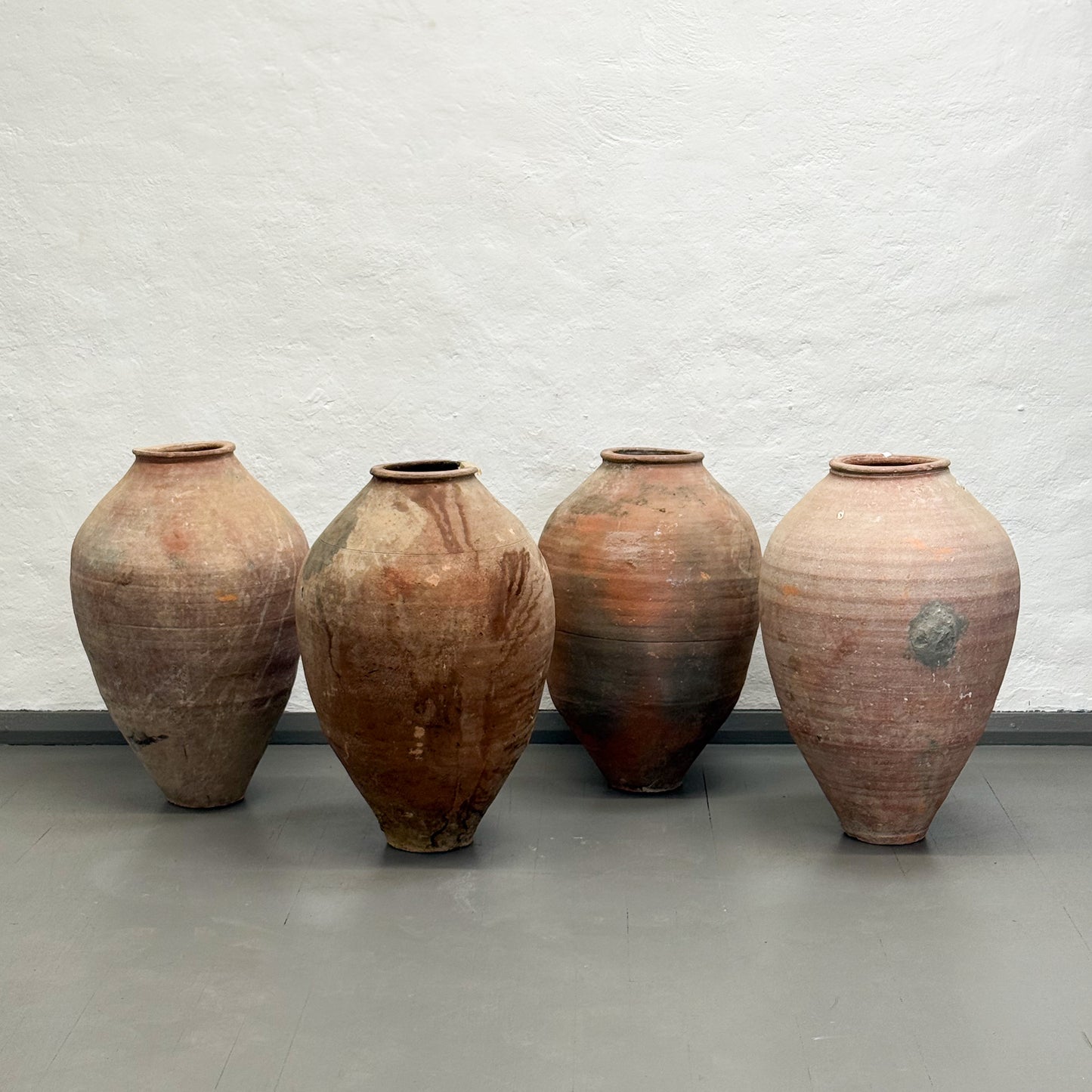 Four large ceramic vases with rustic finishes on a plain floor against a light gray wall.