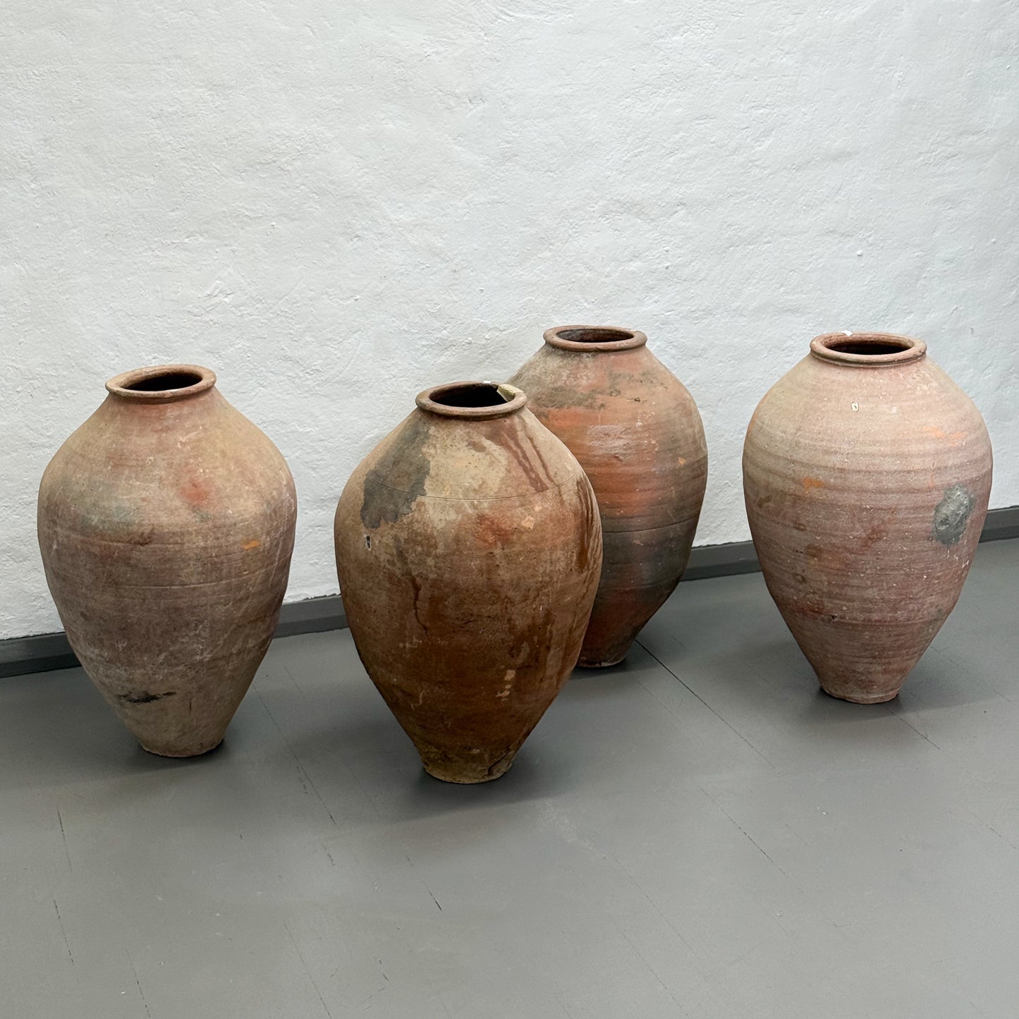 Four large terracotta pots against a plain wall.