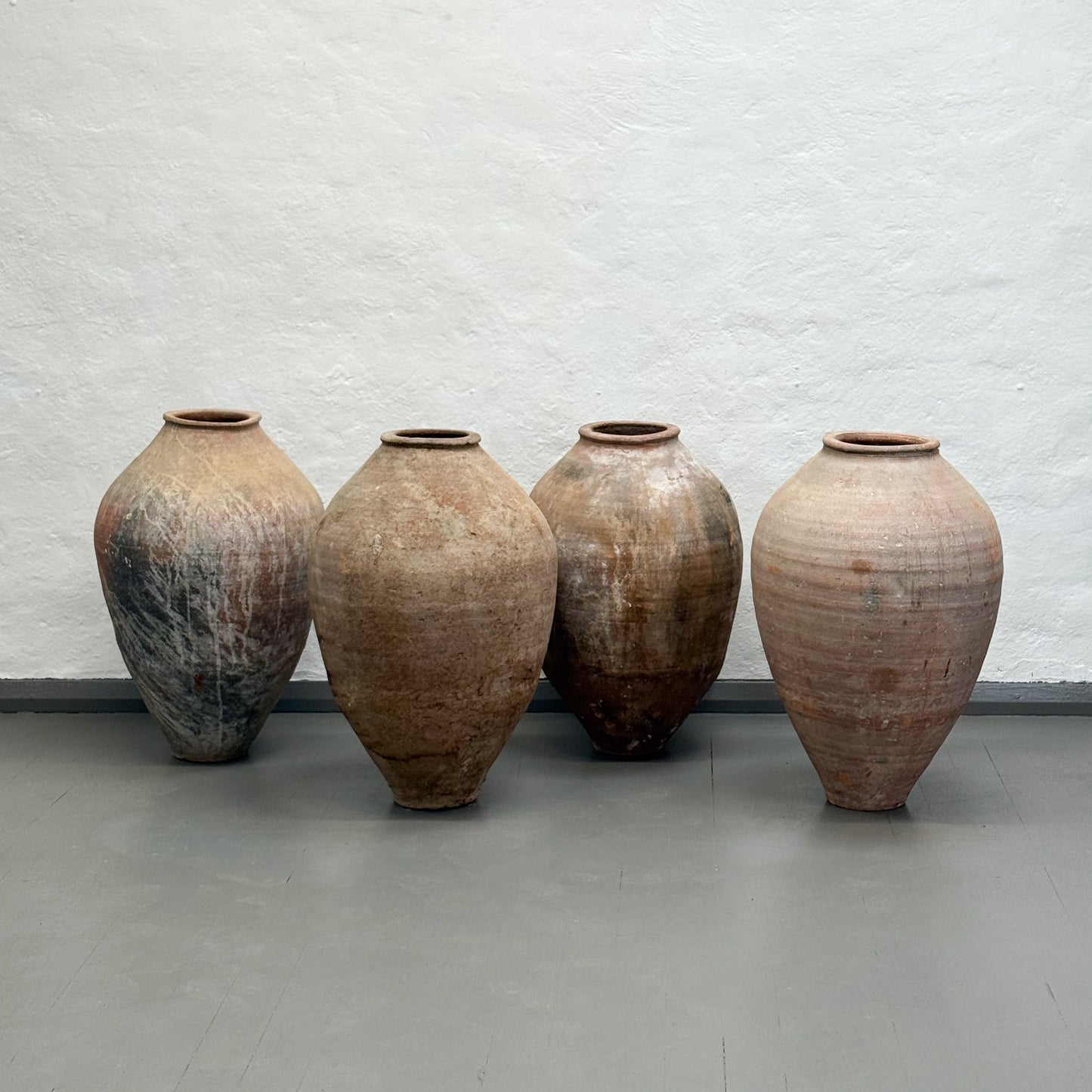Four large ceramic vases of varying sizes against a plain wall.