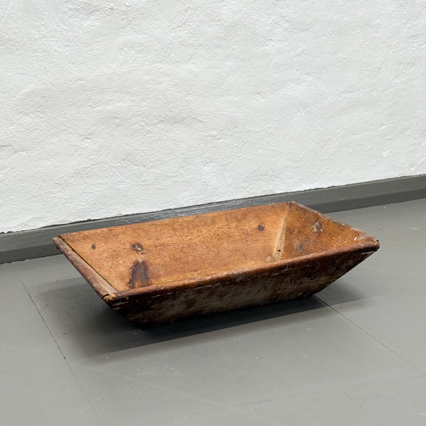 Wooden trough on a gray floor with a white textured wall background