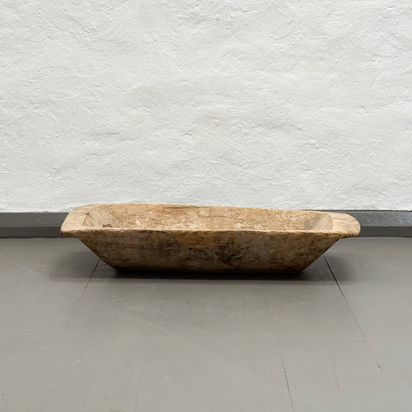 Wooden trough on a gray floor with a textured white wall background