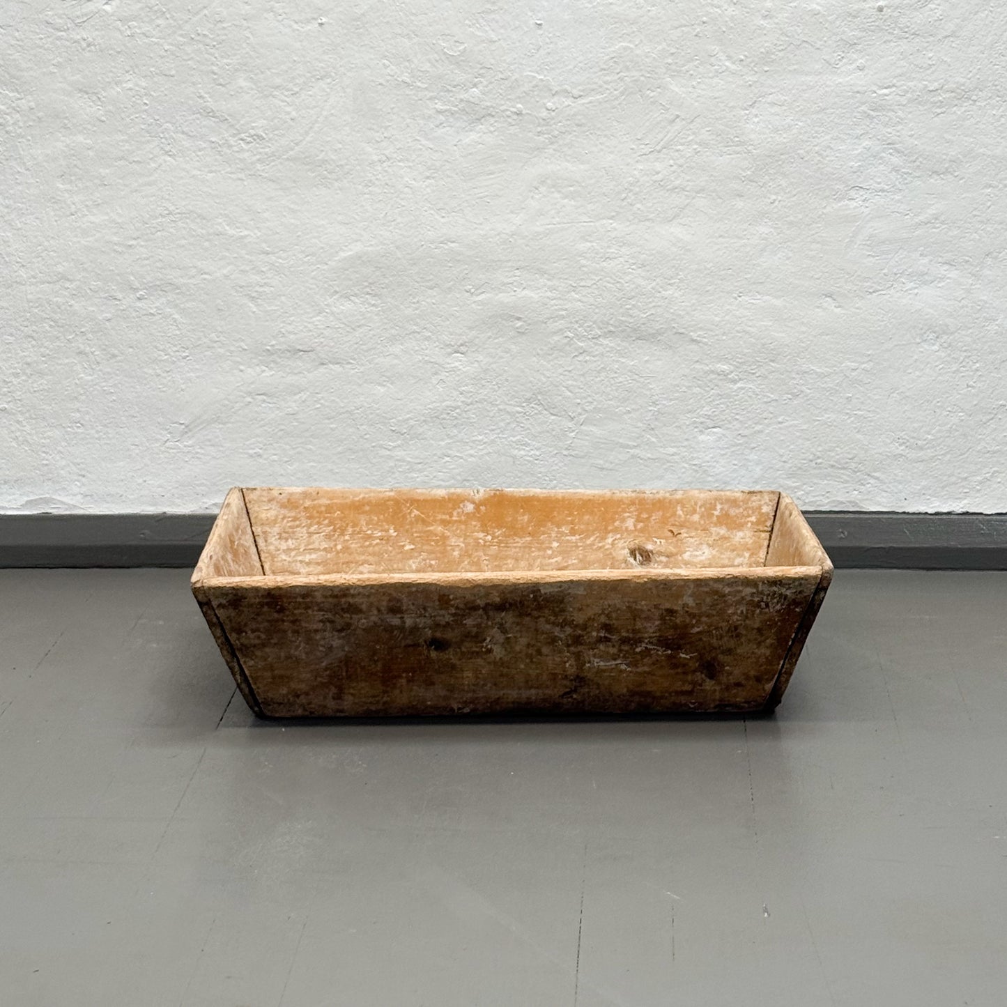 Rectangular wooden trough on a gray floor with a white textured wall background