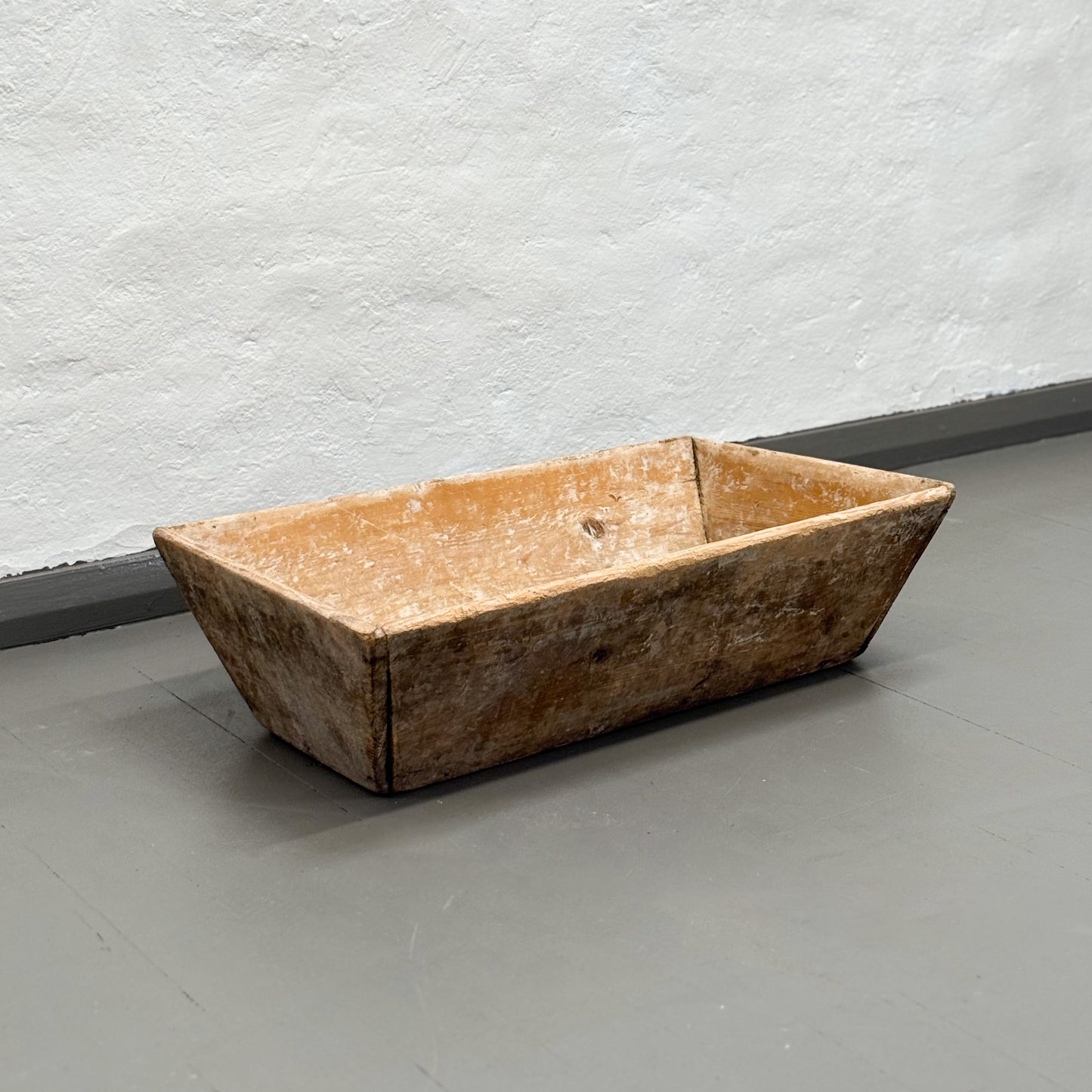 Rustic wooden trough on a gray floor with a white textured wall background