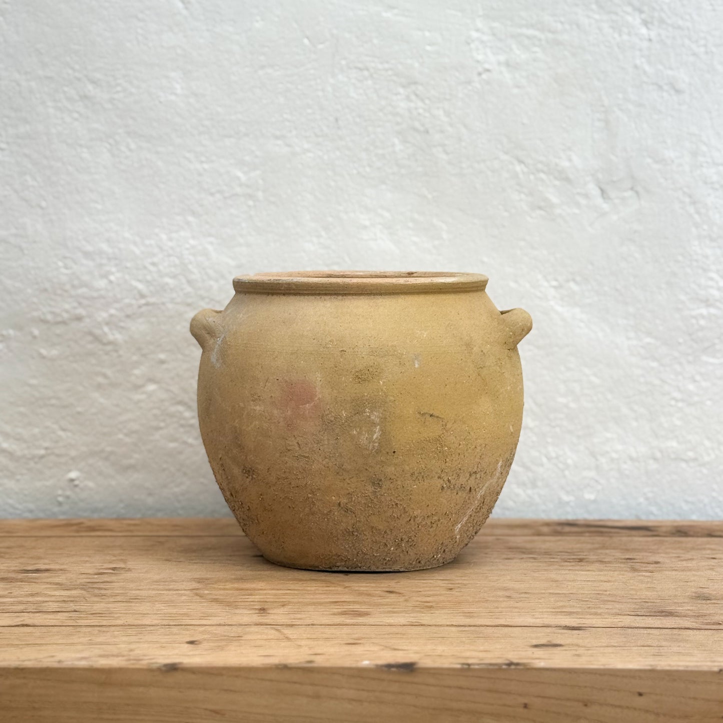 Terracotta pot on a wooden surface with a white textured wall background