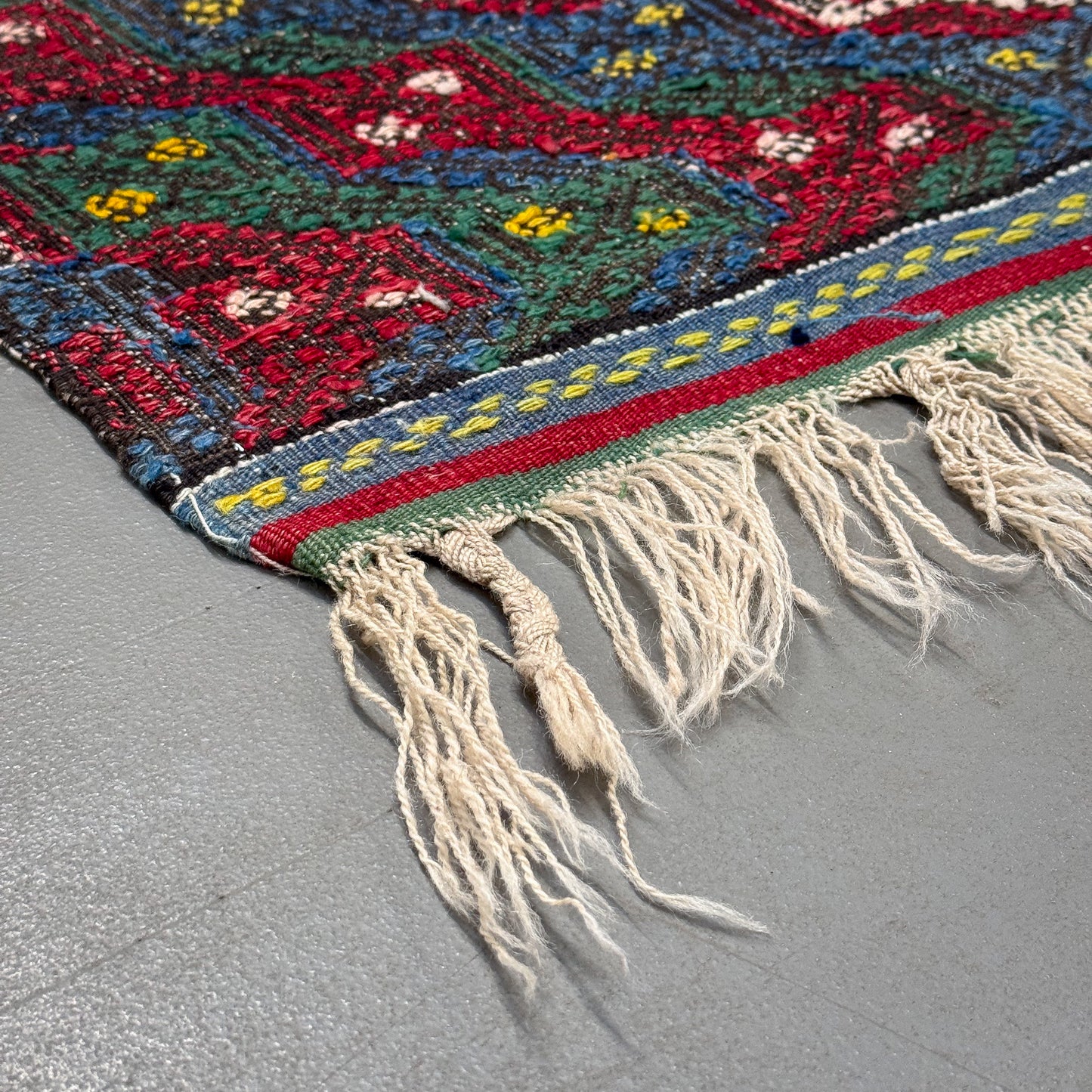 Close-up of a colorful woven textile with fringes on a gray surface