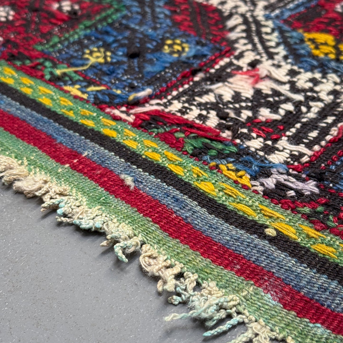 Close-up of a colorful embroidered textile with intricate patterns on a gray background