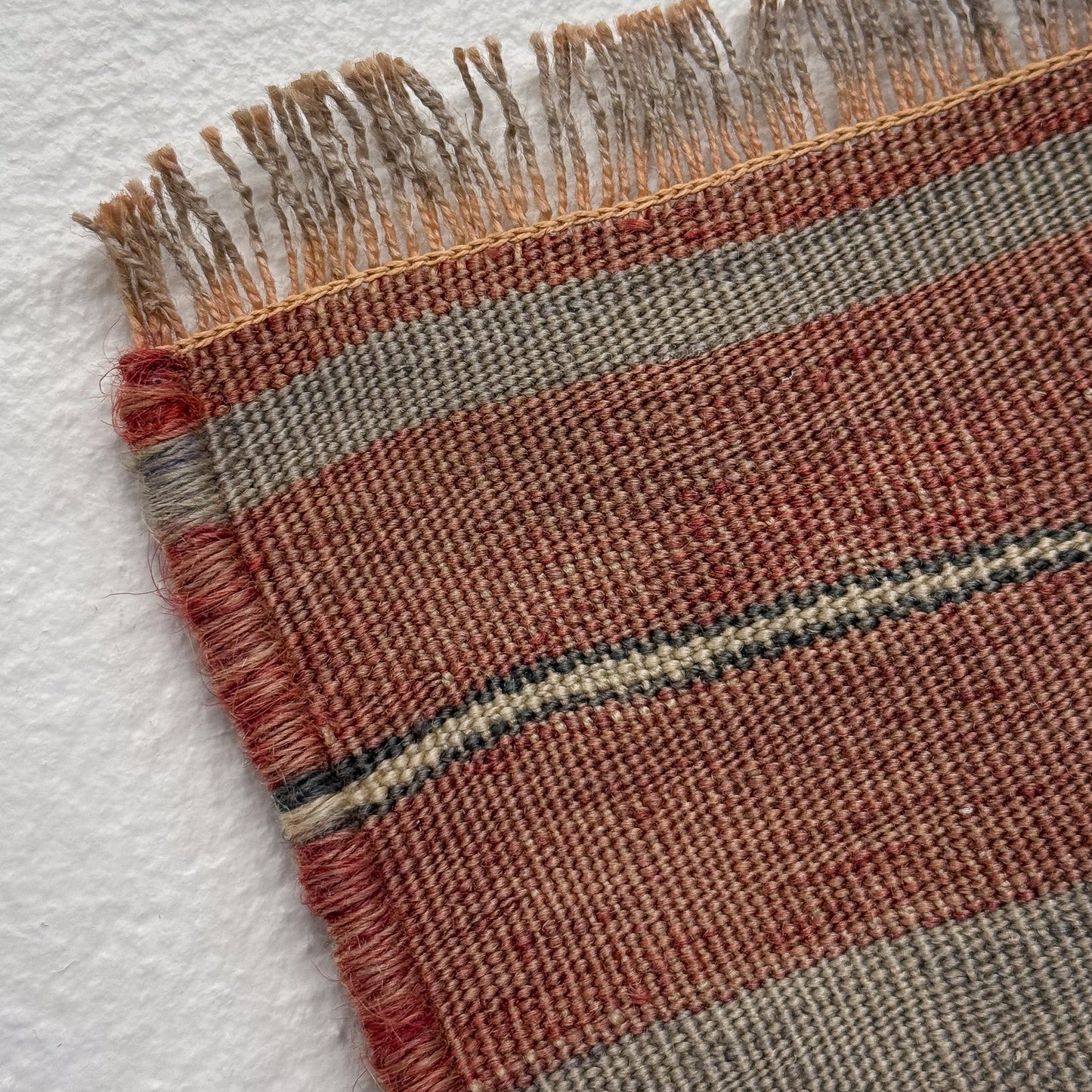 Close-up of a woven textile with fringed edge on a white background