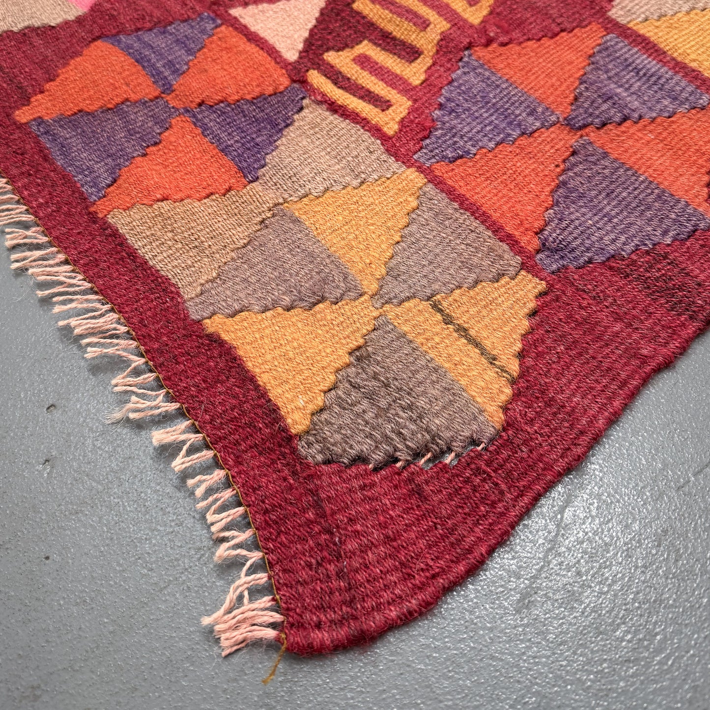 Close-up of a colorful geometric-patterned rug on a gray floor.